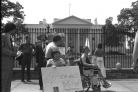 A group of protestors, many are wheelchair users, with Judy Heumann in the forefront holding a handwritten sign that says "Sign 504 regs NOW."