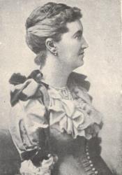 L.T. Meade, the first editor of Atalanta. In this image, she is portrayed in half-body portrait, from head to waist, in a Victorian dress. She is facing almost 90 degrees to the left. Her hair is neatly brushed with small bun. An earring is shown on her right ear.